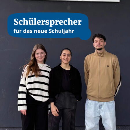 Drei Schüler stehen zusammen vor einer Tafel, um als Schülersprecher für das neue Schuljahr vorgestellt zu werden.