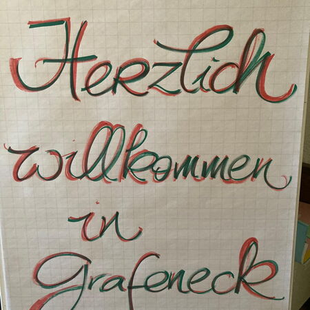 Ein handgeschriebenes Plakat mit der Begrüßung "Herzlich willkommen in Grafeneck" in roter und grüner Schrift.