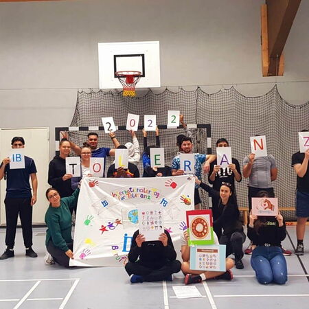 Eine Gruppe von Menschen hält ein Banner und Schilder mit dem Wort "Toleranz" und der Jahreszahl 2022 in einer Sporthalle.