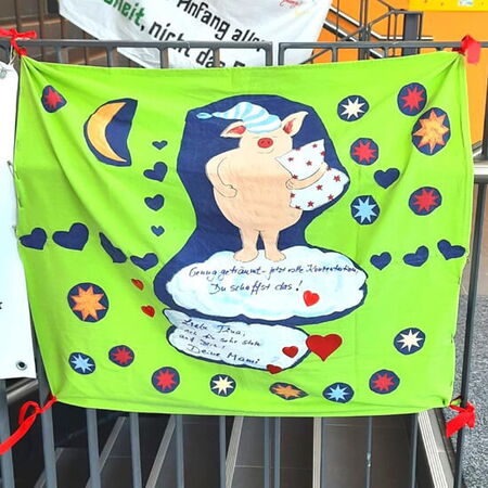 Ein farbenfrohes Plakat zeigt ein Schwein mit Schlafmütze, umgeben von Herzen und Sternen, mit aufmunternder Botschaft.
