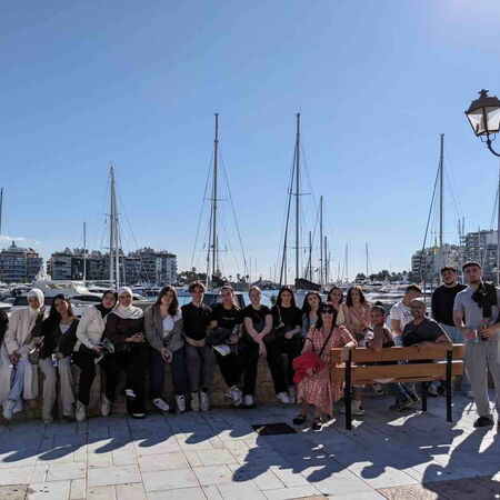 Eine Gruppe von Menschen posiert an einem sonnigen Tag vor einer Reihe von Yachten im Hafen von Athen.