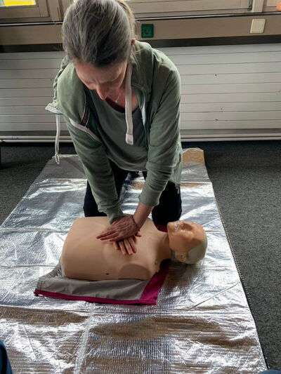 Eine Frau übt Erste-Hilfe-Maßnahmen an einer Puppe auf einer Rettungsdecke während eines PädTag-Workshops.