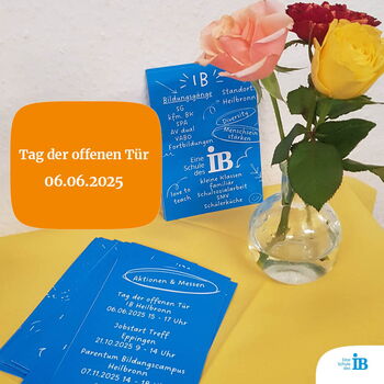 Ein Tisch zeigt Flyer für den Tag der offenen Tür am 06.06.2025, daneben steht eine Vase mit bunten Rosen.
