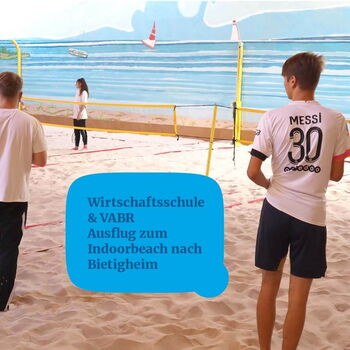 Zwei Personen spielen Beachvolleyball in einer Indoorhalle mit Sandboden und Wandgemälde, während eine dritte Person zuschaut.