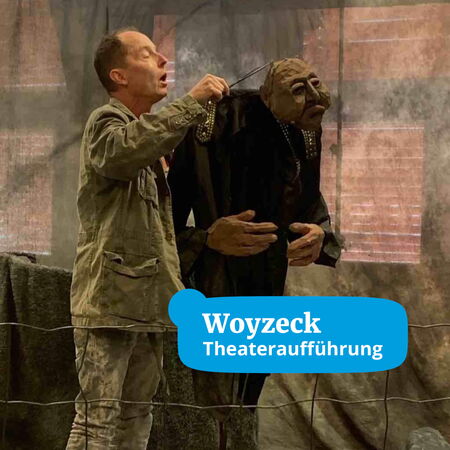 Ein Schauspieler führt während der Woyzeck-Theateraufführung eine große Puppe auf der Bühne.