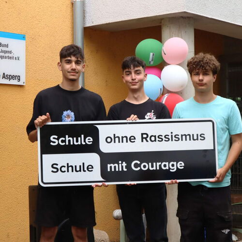 Drei Jugendliche halten ein Schild mit der Aufschrift "Schule ohne Rassismus, Schule mit Courage" vor der Realschule Asperg.