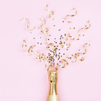 Eine Champagnerflasche auf rosa Hintergrund sprüht goldene Luftschlangen und Sterne zur Feier in die Luft.