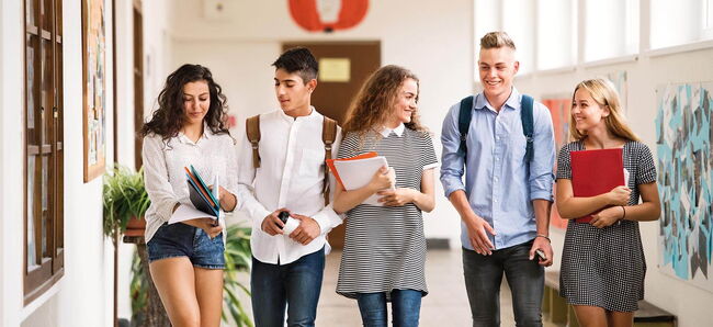 5 Schüler:innen gehen durch einen Flur