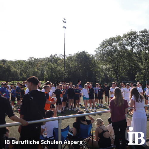 Eine große Gruppe von Jugendlichen versammelt sich bei einem sonnigen Fußballturnier auf dem Sportplatz.