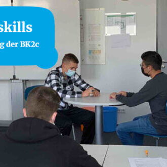 Drei Personen nehmen an einem Softskills-Training in einem Klassenzimmer teil, während zwei von ihnen im Gespräch sind.