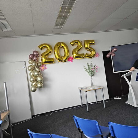 Ein Konferenzraum ist mit goldenen Luftballons in der Form von "2025" und blauen Stühlen dekoriert.