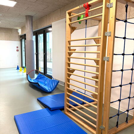 In einer Grundschule steht eine Sprossenwand mit blauen Matten und einem Parcours aus bunten Kegeln bereit.