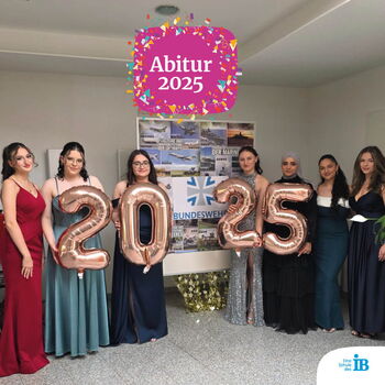Eine Gruppe junger Frauen in Abendkleidern hält Ballons mit der Zahl 2025 bei einer Abiturfeier.