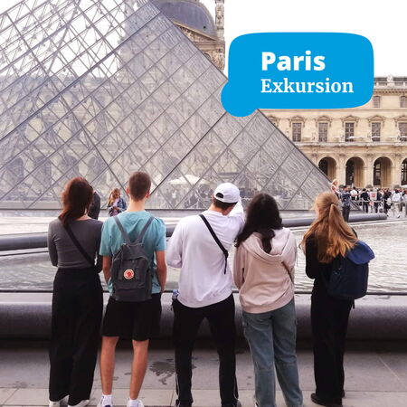 Eine Gruppe von fünf Personen betrachtet die Glaspyramide des Louvre während einer Exkursion in Paris.