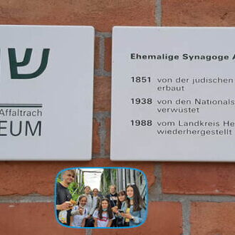 Zwei Tafeln informieren über die Geschichte der ehemaligen Synagoge Affaltrach, begleitet von einem Bild einer fröhlichen Gruppe.