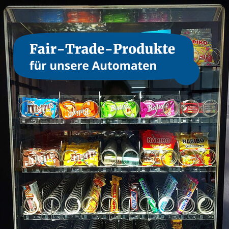 Ein Snackautomat bietet eine Auswahl an Fair-Trade-Produkten, darunter Balisto und Haribo, unter dem Slogan "Fair-Trade-Produkte".