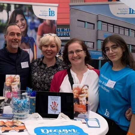 Vier Personen stehen lächelnd an einem Messestand mit Broschüren und Infomaterialien zum Thema Beruf und Bildung.