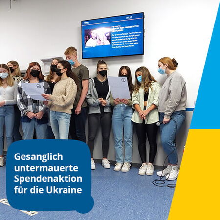 Eine Gruppe junger Menschen singt bei einer Spendenaktion für die Ukraine vor einem Bildschirm im Raum.
