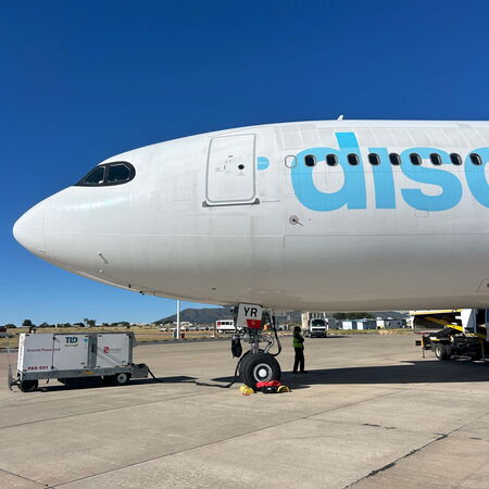Ein Flugzeug steht auf dem Flughafen, während ein Techniker an der Landebein arbeitet und die Sonne scheint.