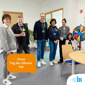 Fünf Personen stehen im Raum beim Tag der offenen Tür, umgeben von einem Glücksrad und informativen Materialien.