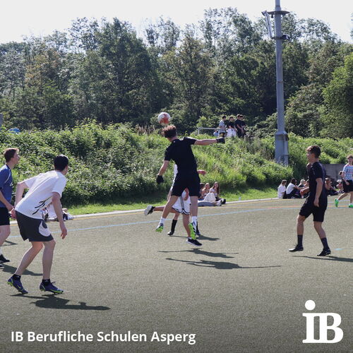 Schüler spielen Fußball auf einem Sportplatz, während ein Spieler den Ball mit dem Kopf trifft.