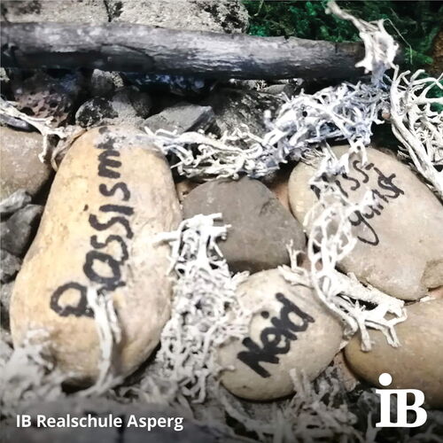 Steine mit den Worten "Rassismus" und "Neid" liegen zwischen Ästen und Moos als Teil eines Wettbewerbsprojekts.