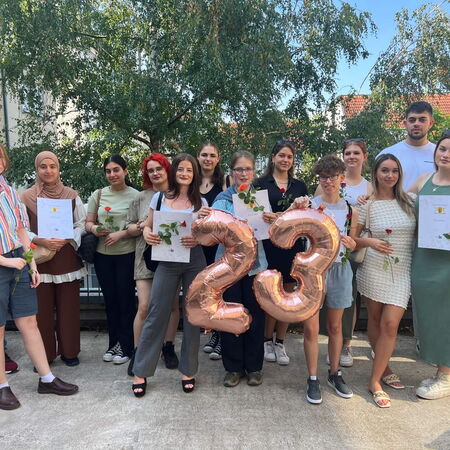 Eine Gruppe von Menschen steht mit Rosen und Zertifikaten zusammen und feiert das Jahr 2023 im Freien.