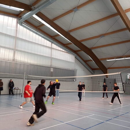Mehrere Personen spielen Volleyball in einer großen Sporthalle mit hohen Decken und einem Netz in der Mitte.