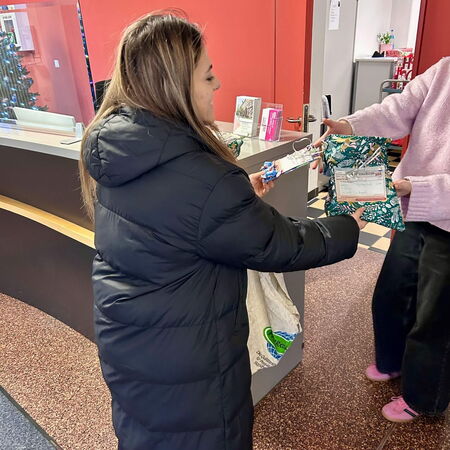 Eine Frau im schwarzen Mantel übergibt Geschenke in einem roten Empfangsbereich an eine andere Person.