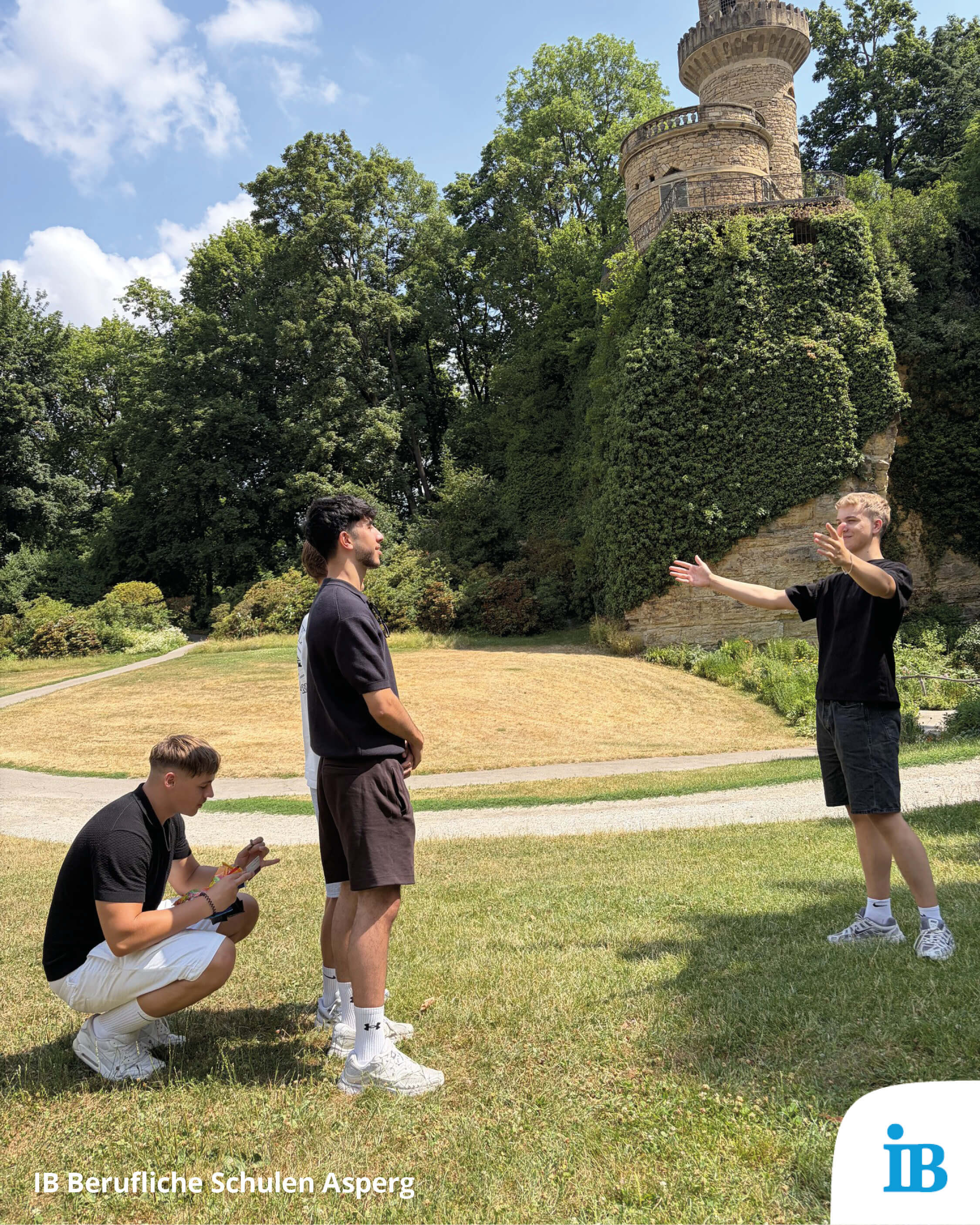 Drei junge Männer stehen im Freien, während einer von ihnen gestikuliert und spricht vor einem märchenhaften Turm.
