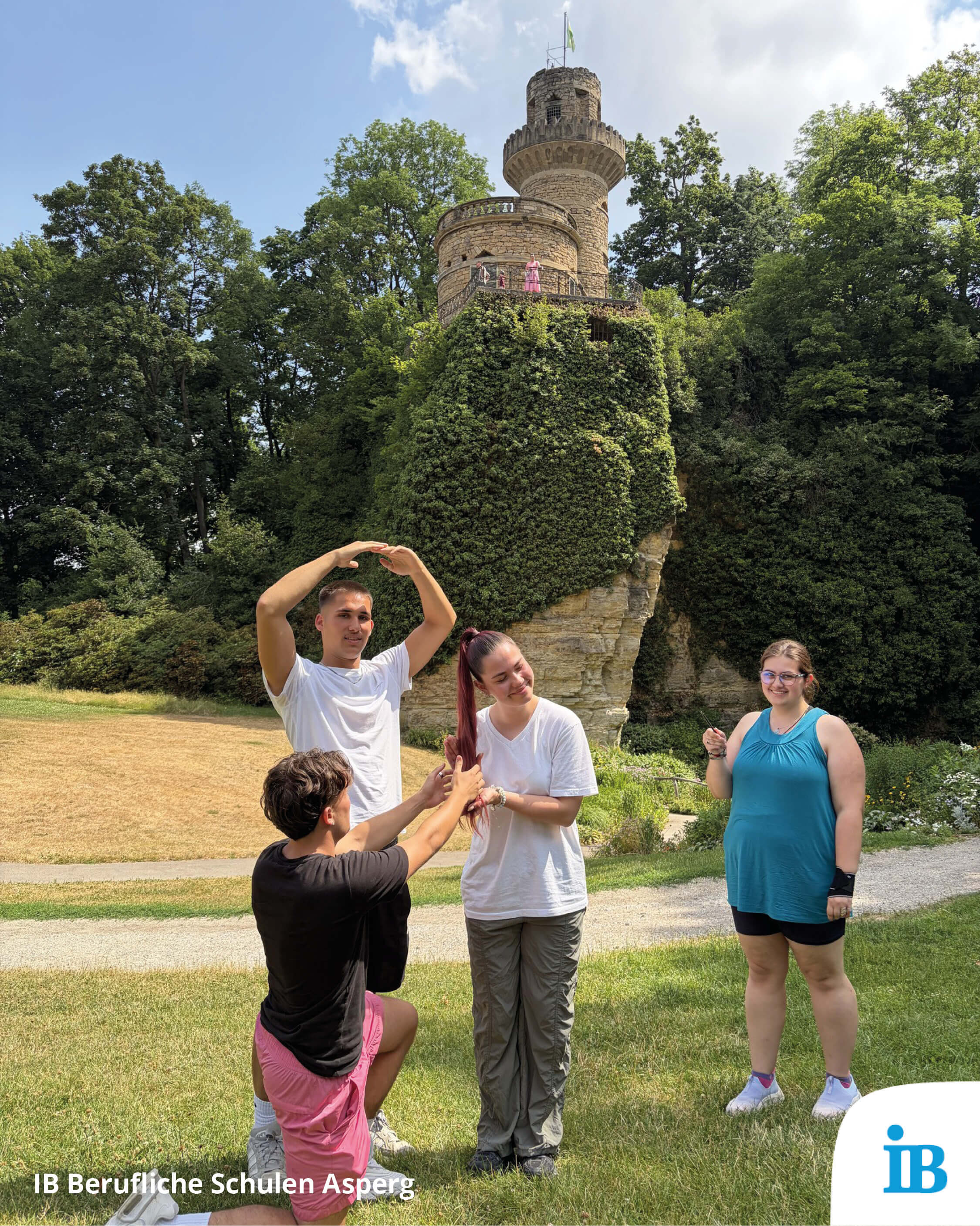 Vier junge Menschen posieren kreativ vor einem märchenhaften Turm in einer grünen Parklandschaft.