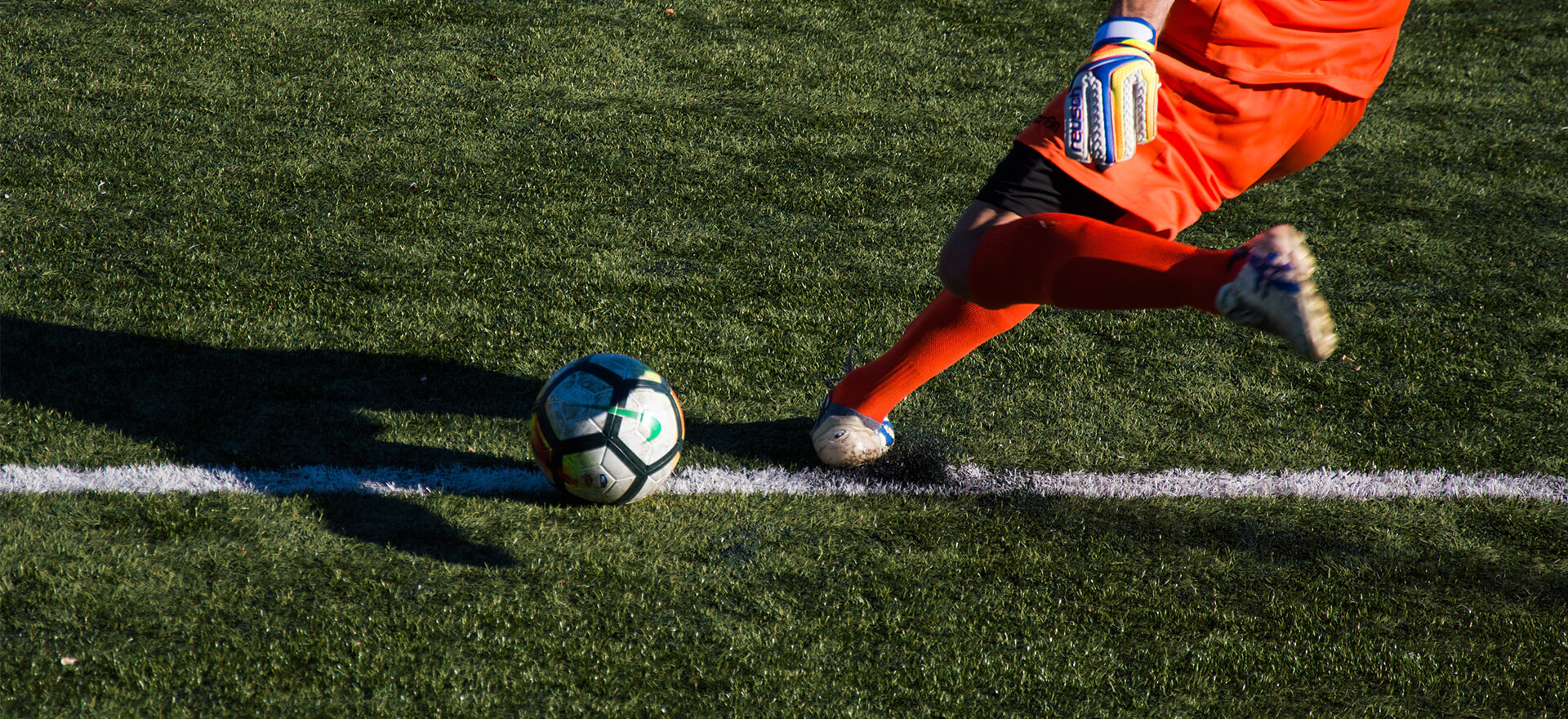Ein Fußballspieler in orangem Trikot schießt den Ball während eines Turniers auf einem grünen Spielfeld.