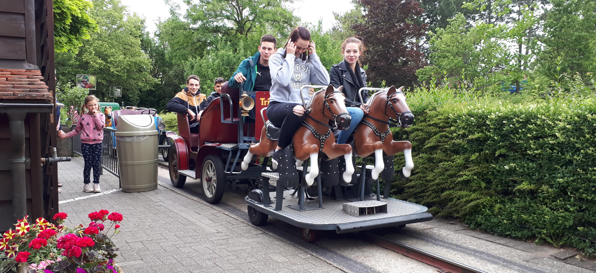 Junge Leute genießen eine Fahrt in einer Kutsche im Freizeitpark Tripsdrill, umgeben von grüner Natur.