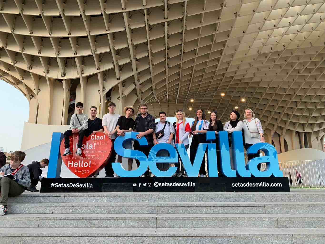 Eine Gruppe junger Menschen posiert fröhlich vor dem "I Love Sevilla"-Schriftzug unter der beeindruckenden Holzkonstruktion.