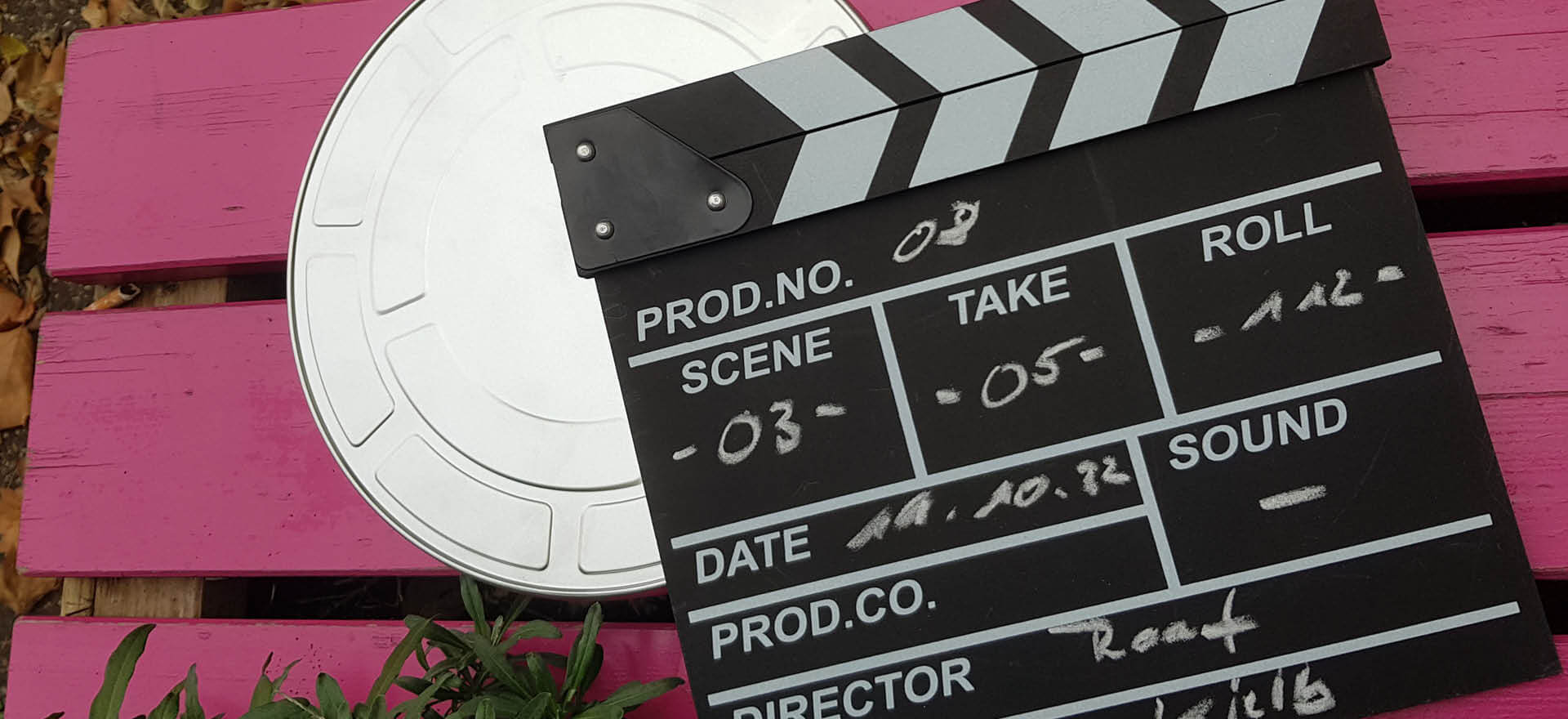 Eine Filmklappe liegt auf einer pinken Bank neben einer Filmrolle, bereit für die nächste Szene.