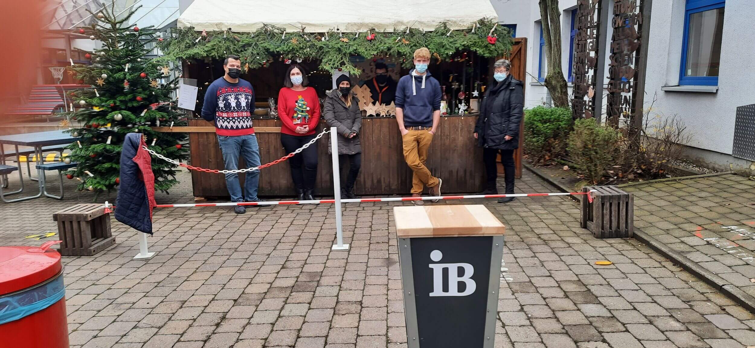 Weihnachtsmarktstand vor der IB Realschule in Asperg, Lehrer*innen und Schüler*innen stehen mit Maske vor dem Stand