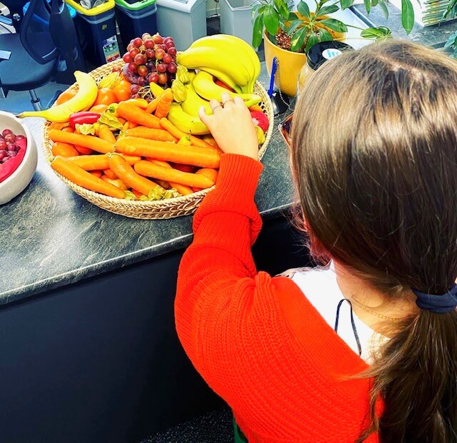 Ein junges Mädchen holt sich Obst aus einem Korb
