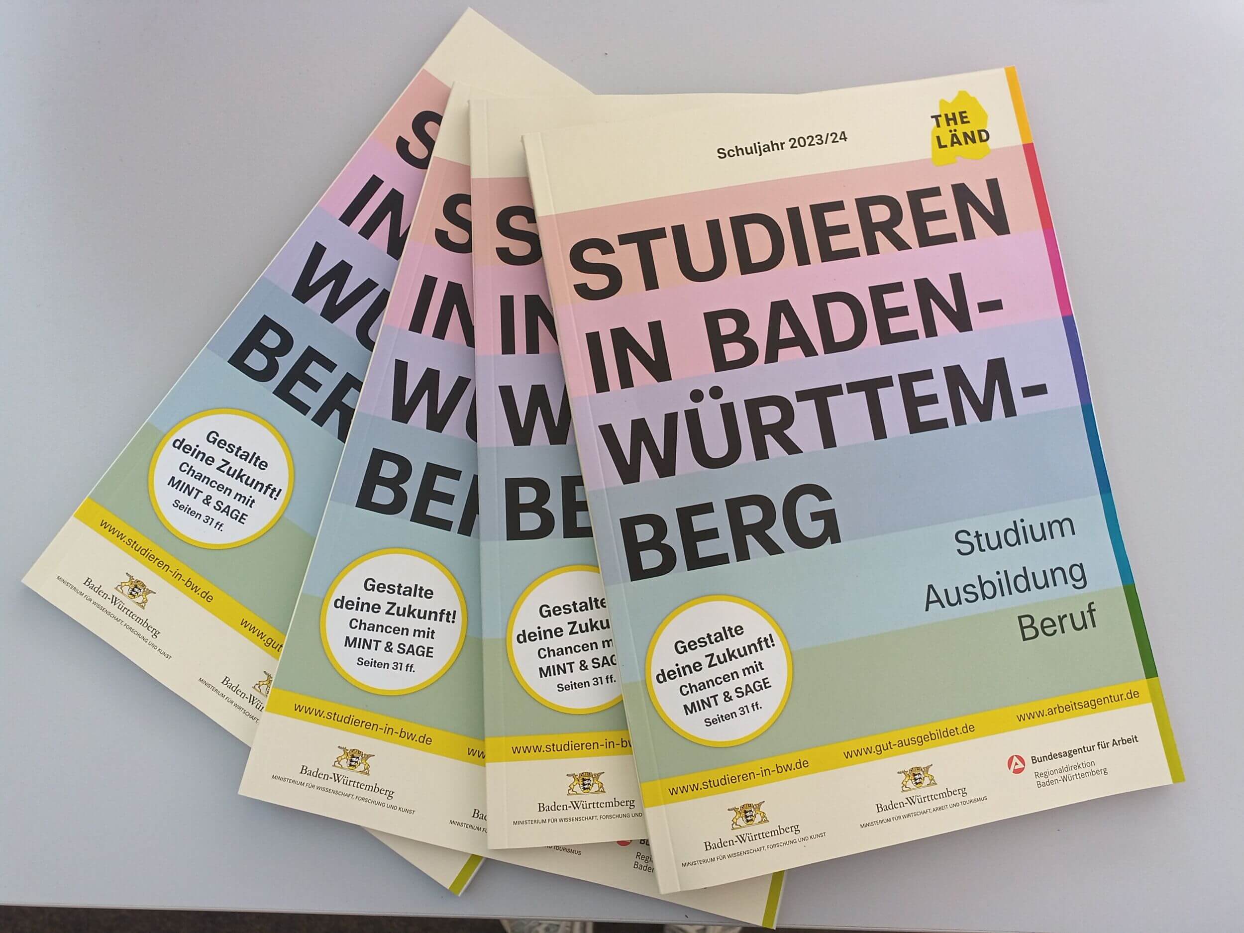 Mehrere Broschüren mit dem Titel "Studieren in Baden-Württemberg" liegen auf einem Tisch, um Bildungsoptionen zu präsentieren.