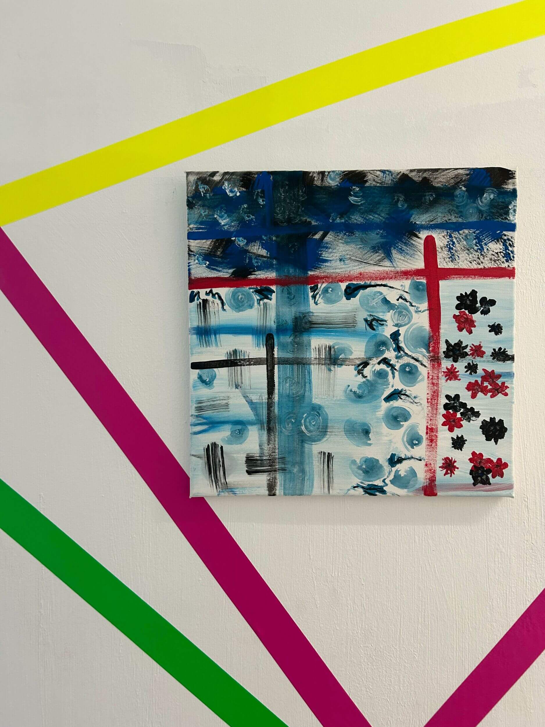 Ein abstraktes Gemälde mit blauen und roten Elementen hängt an einer Wand mit bunten diagonalen Streifen.