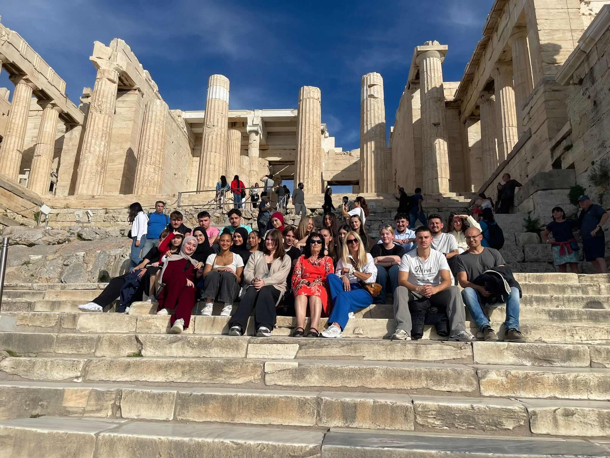 Eine Gruppe von Menschen sitzt auf den Stufen vor dem historischen Parthenon und genießt das sonnige Wetter.