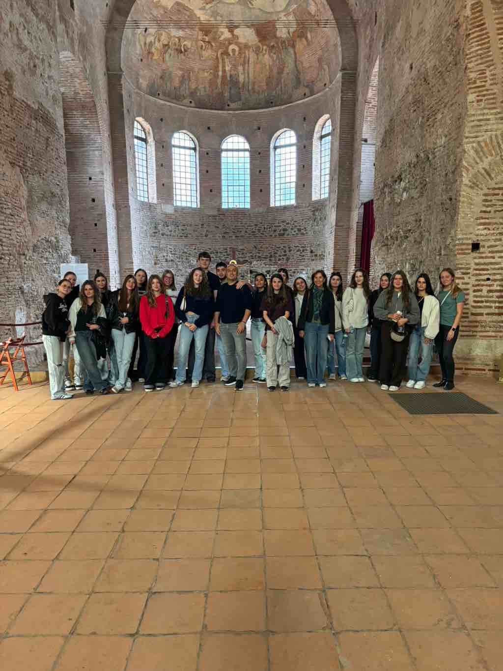 Eine Gruppe steht in einem historischen Gebäude in Thessaloniki mit hohen Fenstern und bemalter Kuppeldecke zusammen.