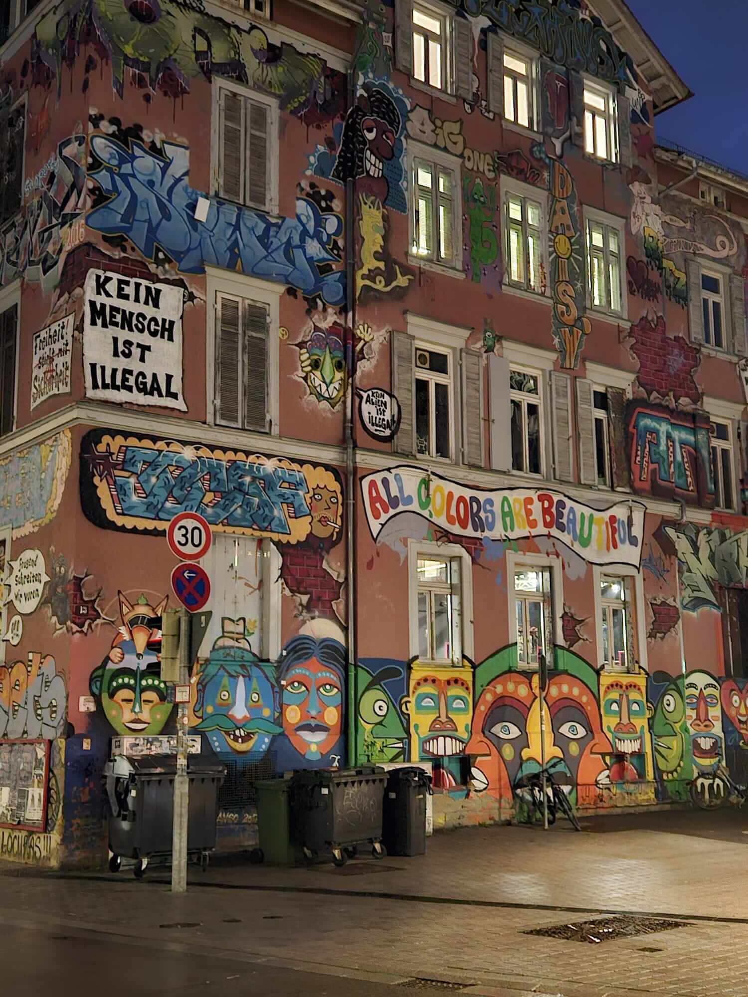 Ein mit bunten Graffiti verziertes Gebäude zeigt die Botschaft "Kein Mensch ist illegal" in leuchtenden Farben.