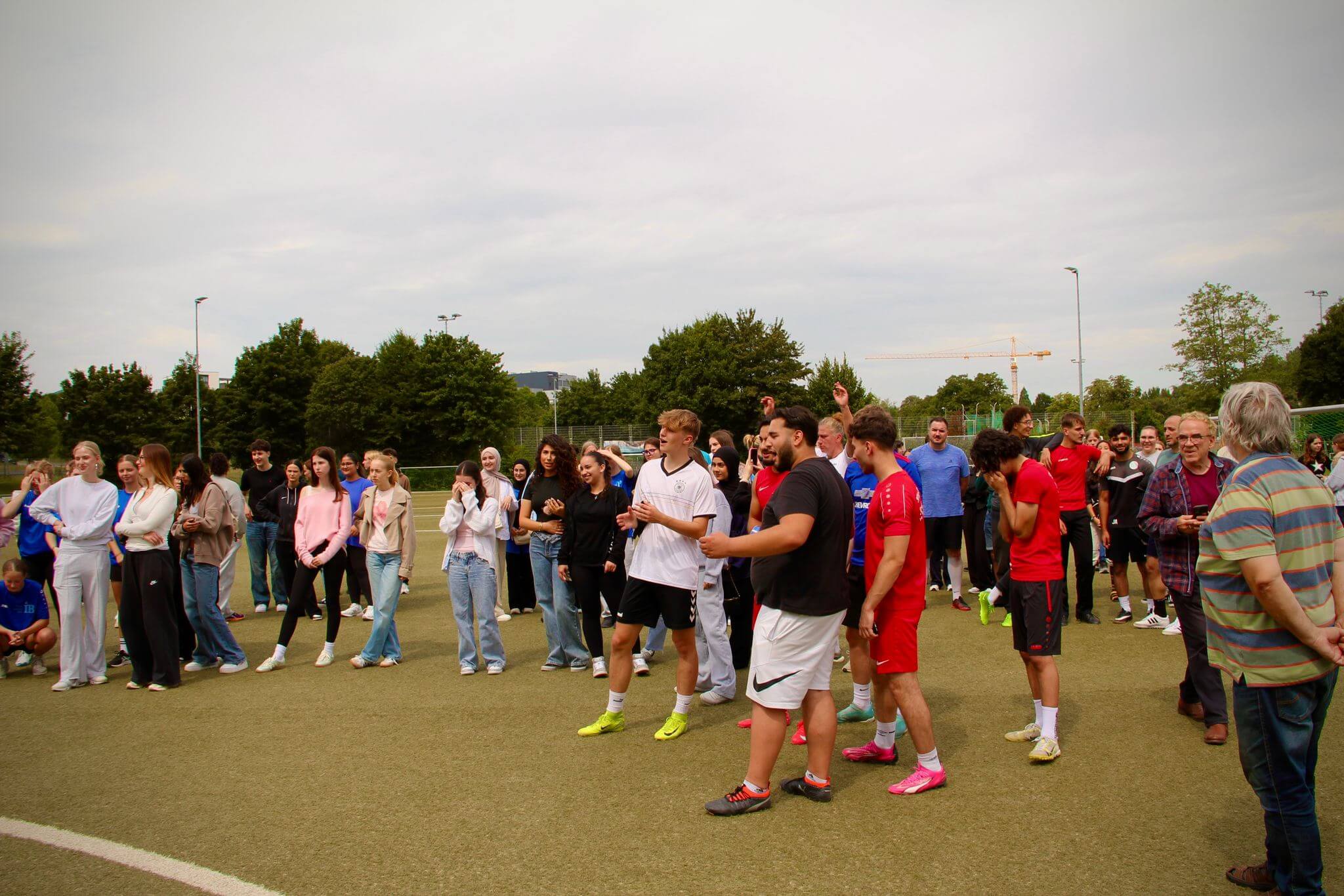 Eine große Gruppe von Menschen versammelt sich fröhlich auf einem Sportplatz bei einer Veranstaltung im Freien.
